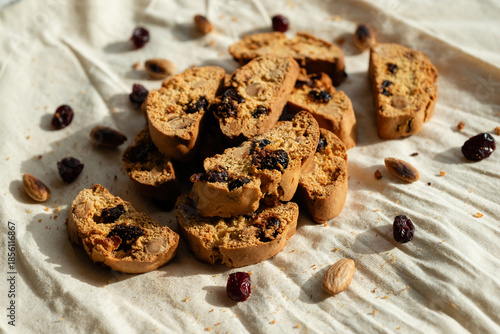 Italian cantuccini biscuits with hazelnuts and cranberries, served on a white linen tablecloth scattered with ingredients