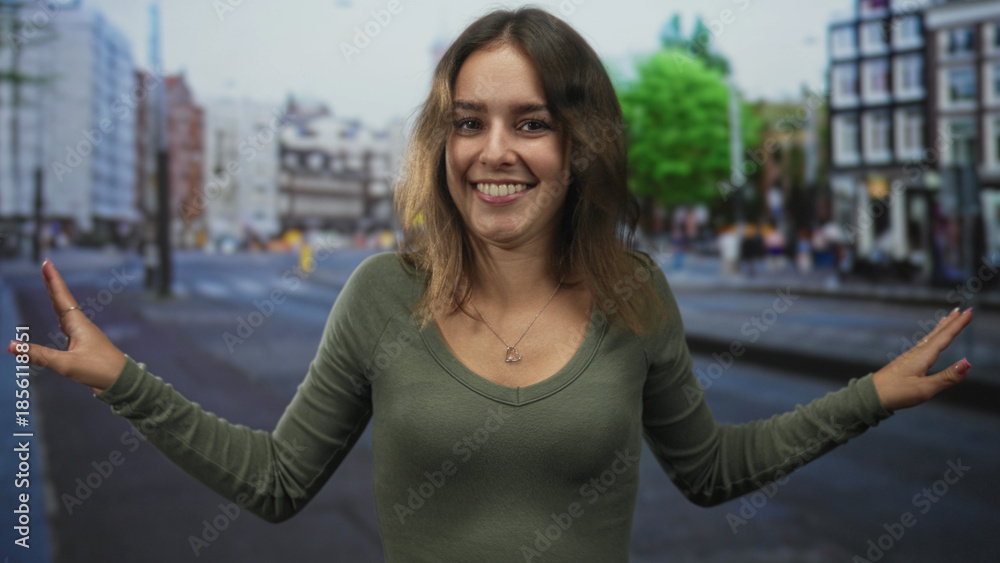 Fototapeta premium Young hispanic woman smiling with hands waving palms forward on a city street crossing wearing green shirt and heart necklace; joy.