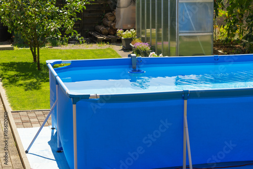 A close-up shot of the clear water swimming pool in the backyard. A beautiful garden with a greenhouse and various plants provides a relaxing area for the whole family during the summer heat.