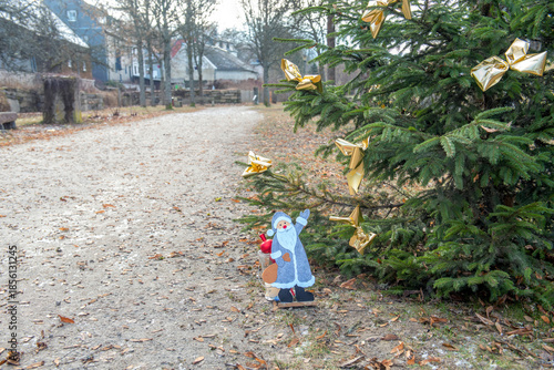 A decorated Christmas tree in a public park of a small German town. Quiet urban setting with autumn leaves and soft holiday lights creates a calm seasonal atmosphere outdoors.