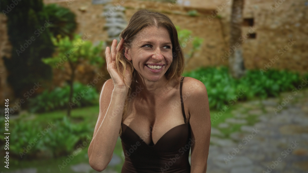 Fototapeta premium Woman with hand to ear listening on old town street while smiling and leaning forward; curious gossip.