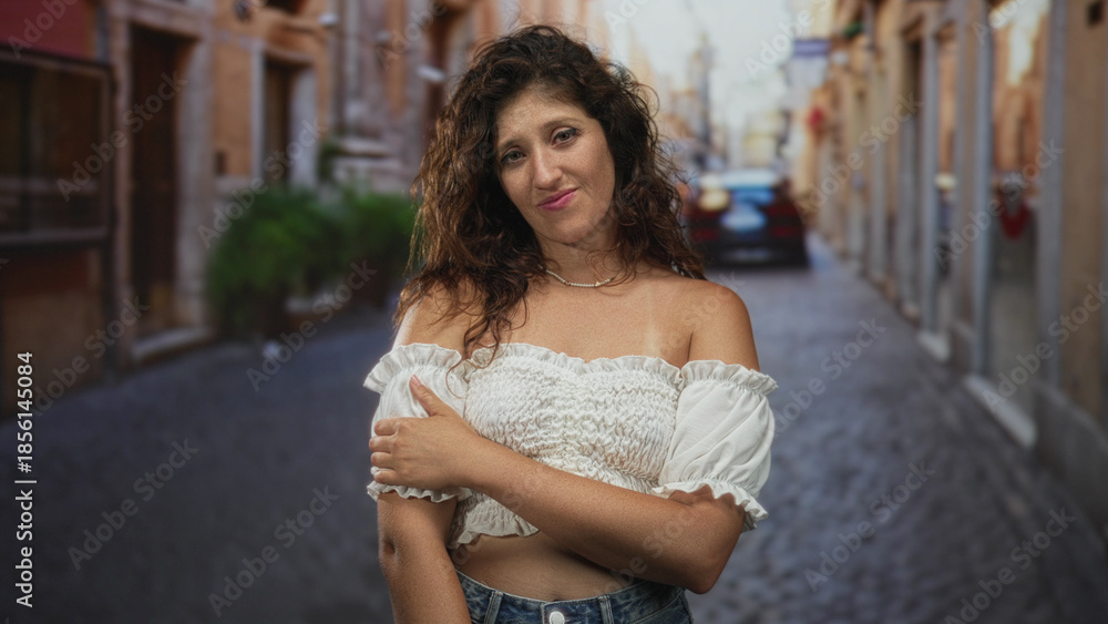 Fototapeta premium Woman holds arm across chest showing shoulder and pearl necklace on cobblestone street; quiet contemplation.