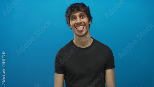 Принти на полотні Young man sticking tongue out against a vivid blue studio wall showing the tongue gesture; playfulness