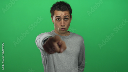 Tableau sur toile Young hispanic man points finger at camera in studio before green wall with stern expression; rejection