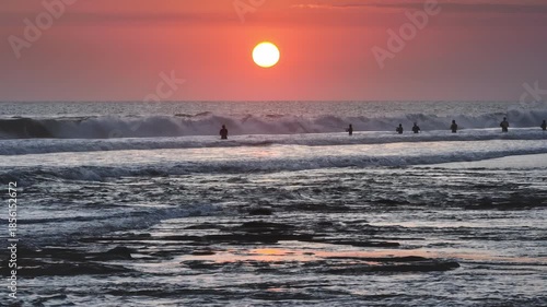Silhouette of fishermen fishing and enjoy tropical evening and active lifestyle. Bright pink light vibrant sky and powerful ocean waves during a beautiful sunset. People recreation on Bali, Indonesia