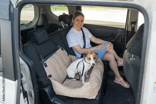 Caucasian woman travels by car with her dog. Jack Russell Terrier in a special car seat. 