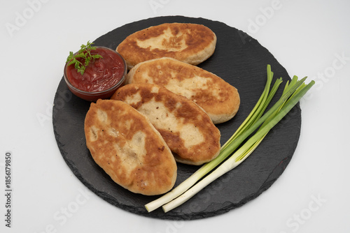 Homemade fried potato pies served with tomato sauce and fresh herbs on black slate plate