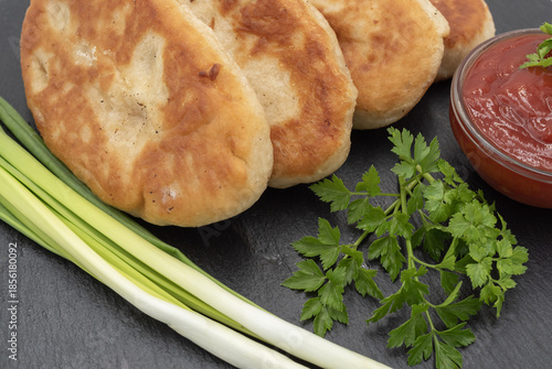 Homemade fried potato pies served with tomato sauce and fresh herbs on black slate plate