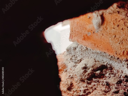 A gritty close-up through a brick opening reveals dusty ground and rubble at a construction site,