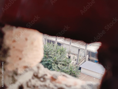 A gritty close-up through a brick opening reveals dusty ground and rubble at a construction site,