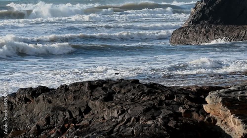 Ocean waves washing over coastal rocks with foamy water and wet stone texture in Portugal. Close view of shoreline detail with moving water and natural coastline