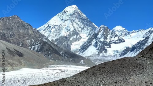 A majestic snow-capped mountain dominates the scene with others flanking it under a clear sky