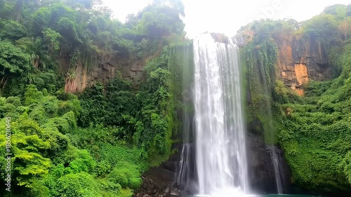 A tall waterfall plunges into a pool, lush vegetation covers the cliffs around it