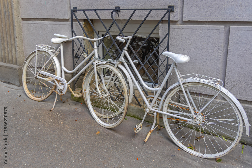 Obraz premium Two Old White Bicycles Chained to Window Bars at Street Decor