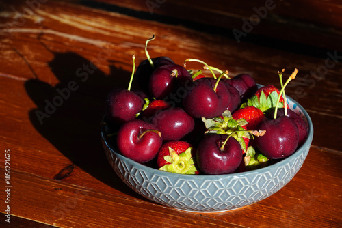 Delicious fresh cherries and strawberries sit in a bowl on a wooden table