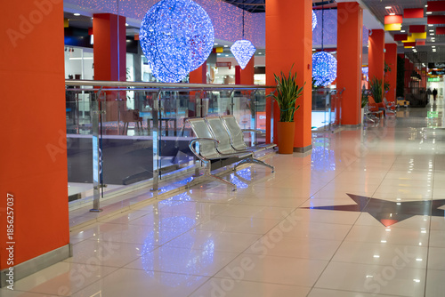 Fotografia Bright lights hang from the ceiling while benches sit empty in a shopping mall c