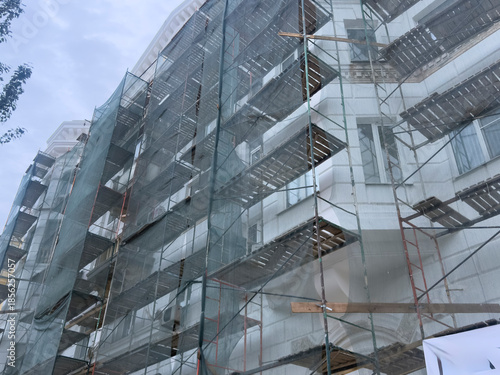 Workers prepare to renovate the building wrapped in scaffolding and mesh near the street