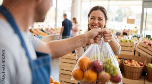 Happy woman buying fresh fruit bag from shop assistant in grocery store market.
