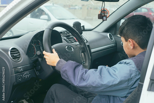 Φωτογραφία A young boy, engrossed in the act of pretending to drive, sits behind the steering wheel inside a parked car, seemingly lost in his imagination