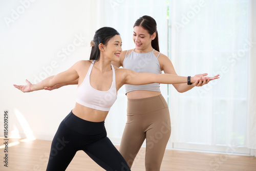 Women practicing yoga together with arms outstretched for balance, helping and supporting each other