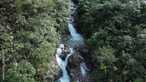 Crystal clear water flows through a rocky mountain stream, surrounded by lush green trees along its banks. This scene captures the natural beauty of the Papuan jungle, Indonesia.