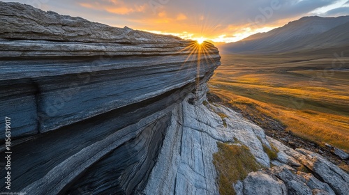 Dramatic sunset illuminates textured layered rocks on a rugged mountain landscape