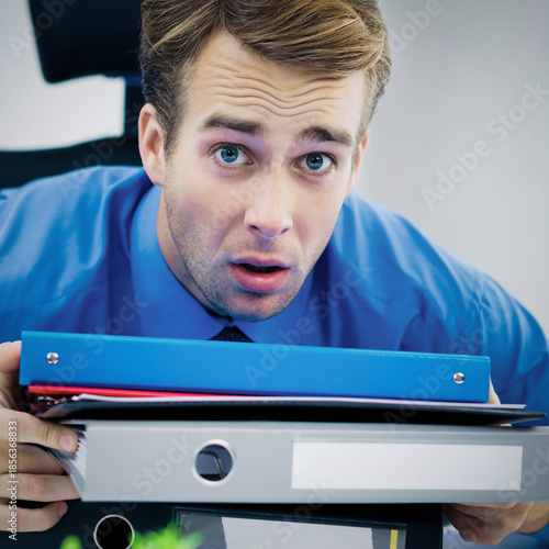 Image of under stressed shocked business man wear blue shirt, tie with folders of documents, at office. Job, occupation and overworking concept. Square composition