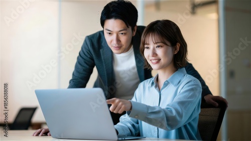 PC画面を指差し情報を共有するオフィス内の男女