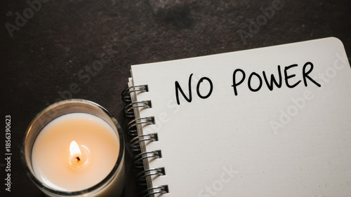 Notebook with no power message and candle on desk during winter blackout emergency at home