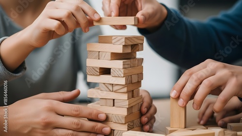People's hands carefully stack wooden blocks to build a tower during a game