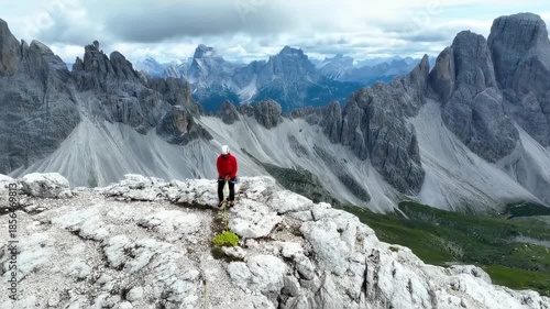 A mountain climber stands atop rocky peak, with a mountainous backdrop