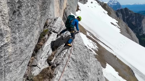 A climber traverses a rocky mountain face with snowy peaks in the background