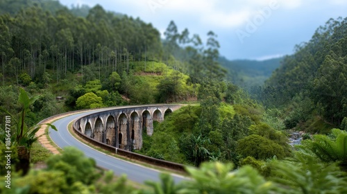 Scenic winding road through lush green hills with historic stone bridge and cloudy sky in serene landscape setting