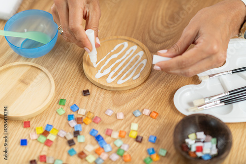 Female hands adding glue while designing decorative coasters. Highlights coordination, slow craft rhythm, and structured artistic technique.