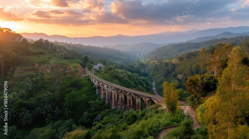 Scenic Bridge Over Valley at Sunset with Lush Green Surroundings and Majestic Mountains in Background