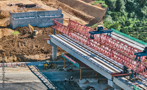 Fotografi Bridge Construction Site with Red Steel Girders and Heavy Equipment