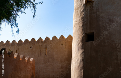 Close-up of Al Zubara Fort in Qatar, showcasing sand-brick walls, triangular battlements, and a cylindrical tower under bright sunlight and a clear blue sky.