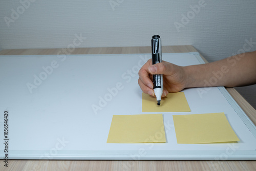 фотографія Hand writing on a sticky note on a white board with a black marker