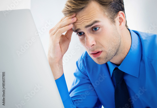 Shocked stressed concerned about what he sees on monitor businessman man wear blue shirt, tie. Work looking at computer screen with worried expression at office. Business, overload, job concept