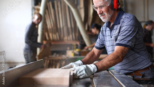 Senior carpenter cutting wood plank using industrial saw