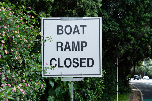 Boat Ramp Closed roadside sign.  Black lettering on white sign, on a metal stand.   Road in the background. 