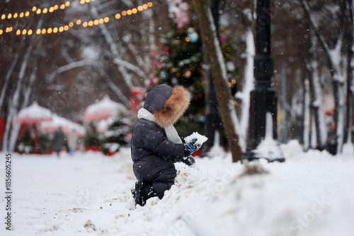 Child playing in snow in winter park on New Year decoration background