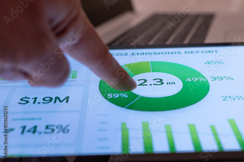 Hand pointing at a digital dashboard showing co2 emissions report with pie chart and financial data, analyzing corporate esg metrics for sustainable strategy and investment decisions