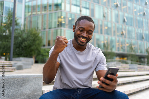 Photos Happy African American man euphoric winner with smartphone on street in city