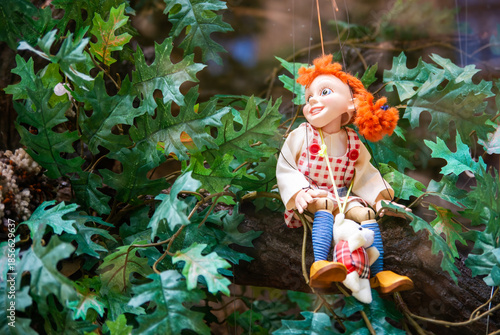 A wooden string puppet girl with red head, green foliage background