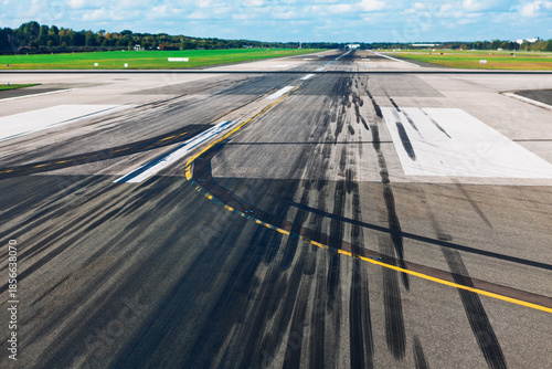 Black skid marks streak across a worn runway, framed by white and yellow aviation lines. Runway pavement featuring prominent dark rubber deposits indicating recent high-stress braking or maneuvering