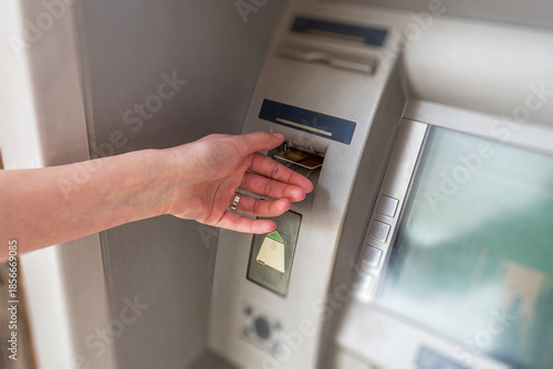 A person's hand inserting a credit card into an automated teller machine to perform a banking transaction.