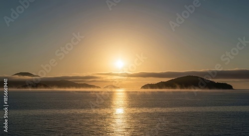 Calm sunrise over misty islands, golden light reflecting on tranquil water