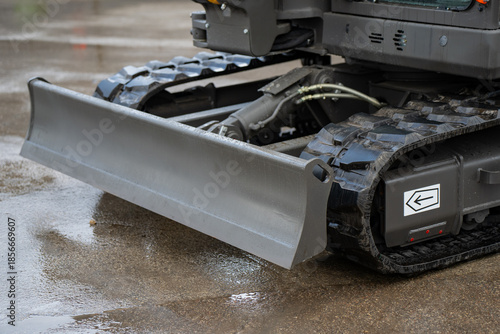 Industrial excavator undercarriage featuring front dozer blade and tracked drive system on paved ground, focused on construction machinery durability