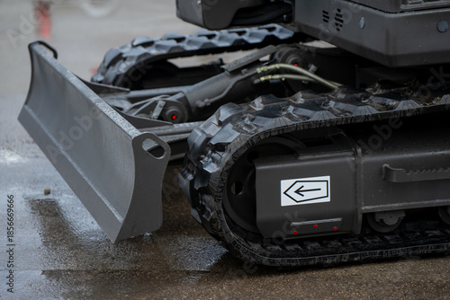 Tracked construction excavator detail showing front blade, rubber track system, and hydraulic components, emphasizing heavy machinery design and durability